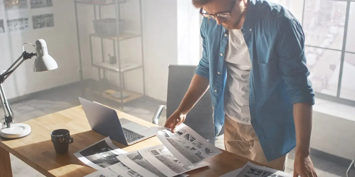 A designer at his desk sorting through some UI storyboards on sheets.