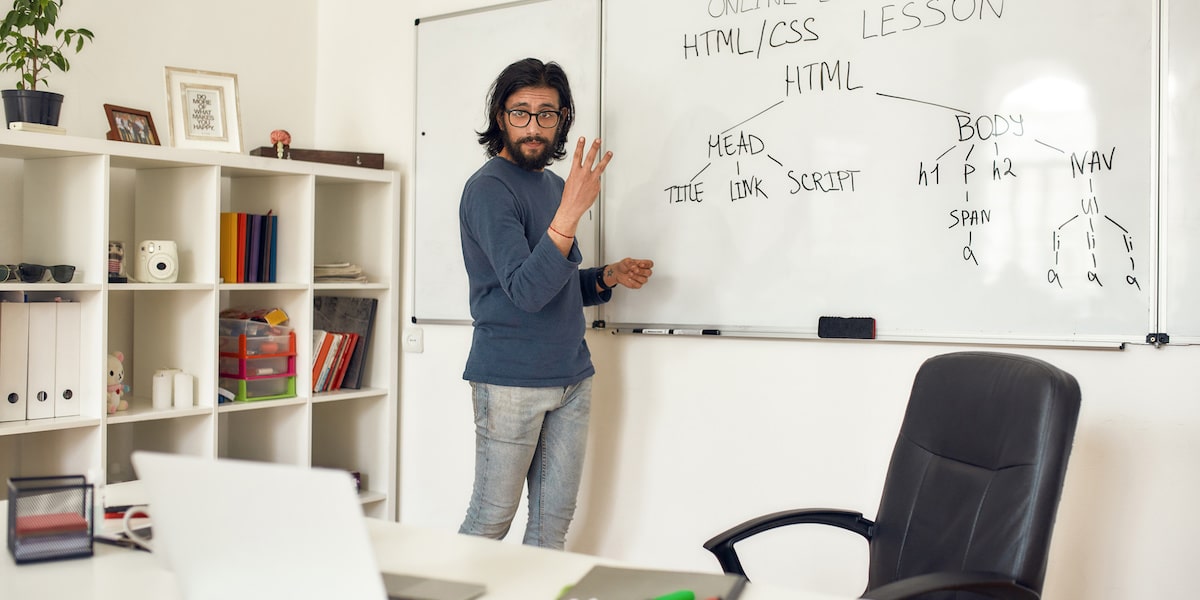 一位在线编码类教师站在白板前正视笔记本教学HTML和CSS