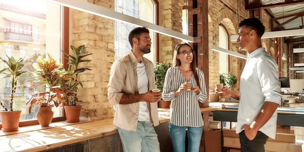 A man in an office stands with coffee asking his colleagues how to become a software engineer without a degree.