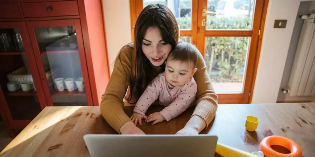 A young mother enjoys the benefit of remote work while at laptop with baby