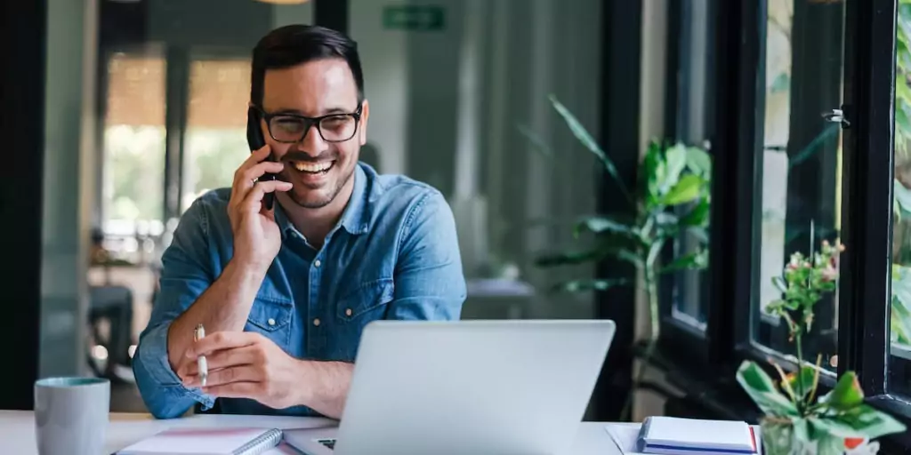 smiling businessman uses soft skills while on the phone with his laptop in front of him