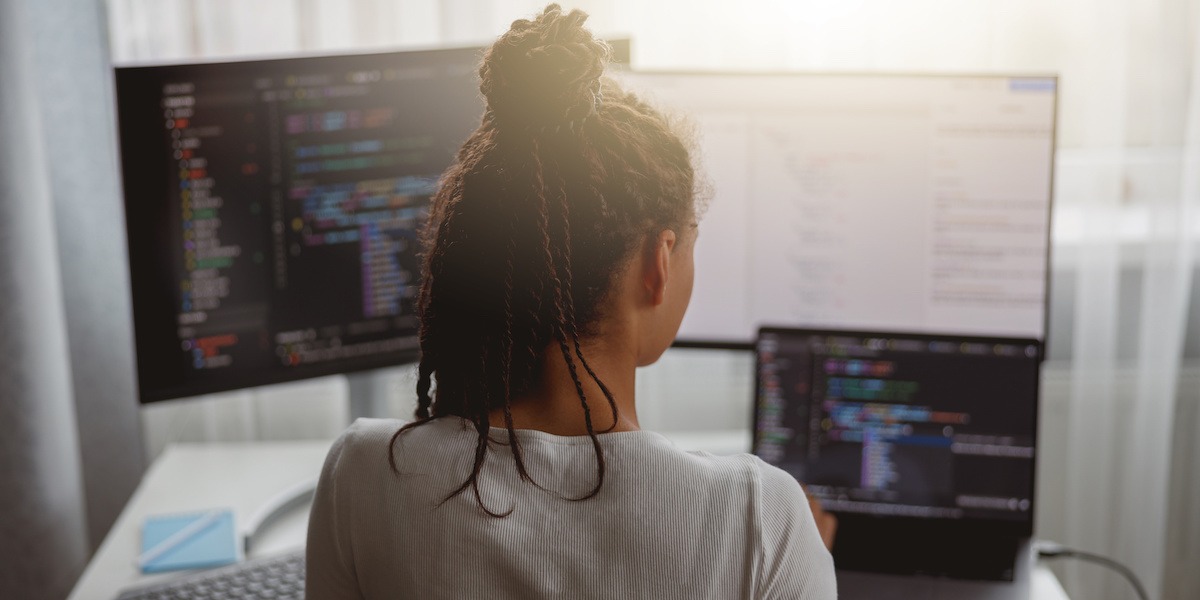Woman taking a JavaScript bootcamp works on her desktop computer with three screens of JavaScript code.