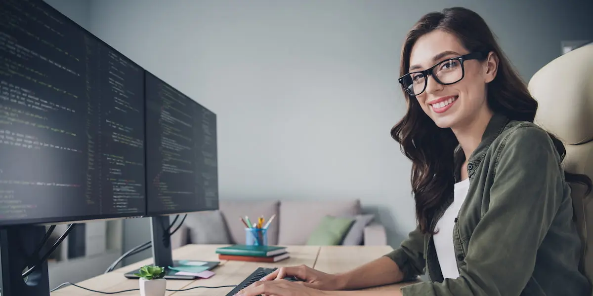 a web developer works at her tech job on her computer while looking at the camera