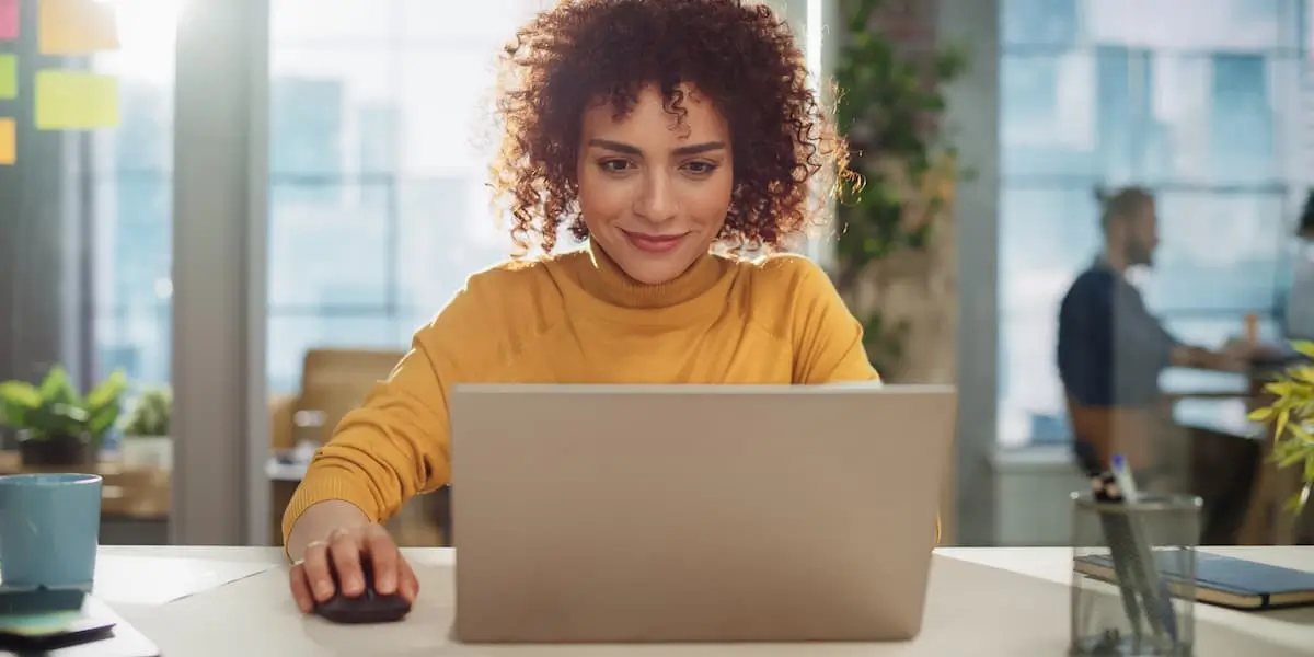 young woman looks at her laptop with mouse in hand