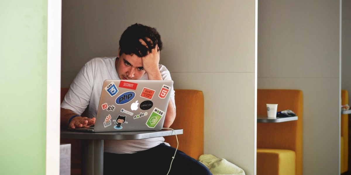 A man sitting at an office workstation with his hand on his head, staring at his laptop in frustration