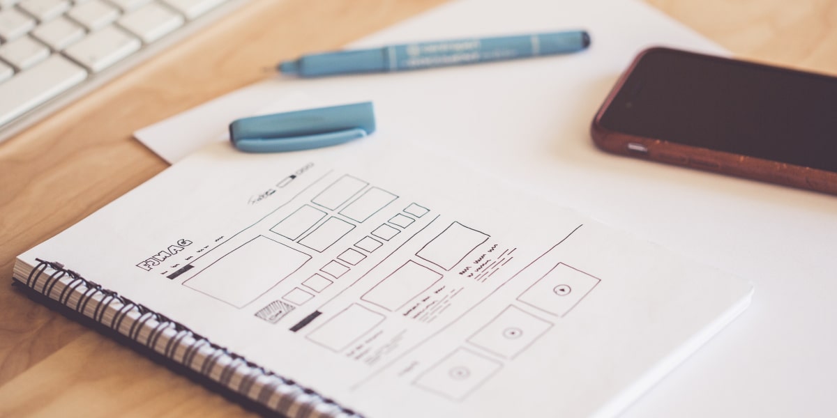 A phone and pen resting on a notebook UX wireframe sketches