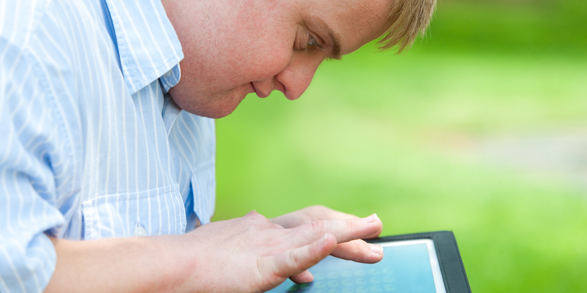 A man sitting in a park, working on a tablet