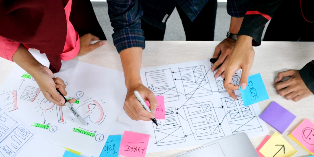 UX designers hands at work around a desk, organizing user research into a prototype