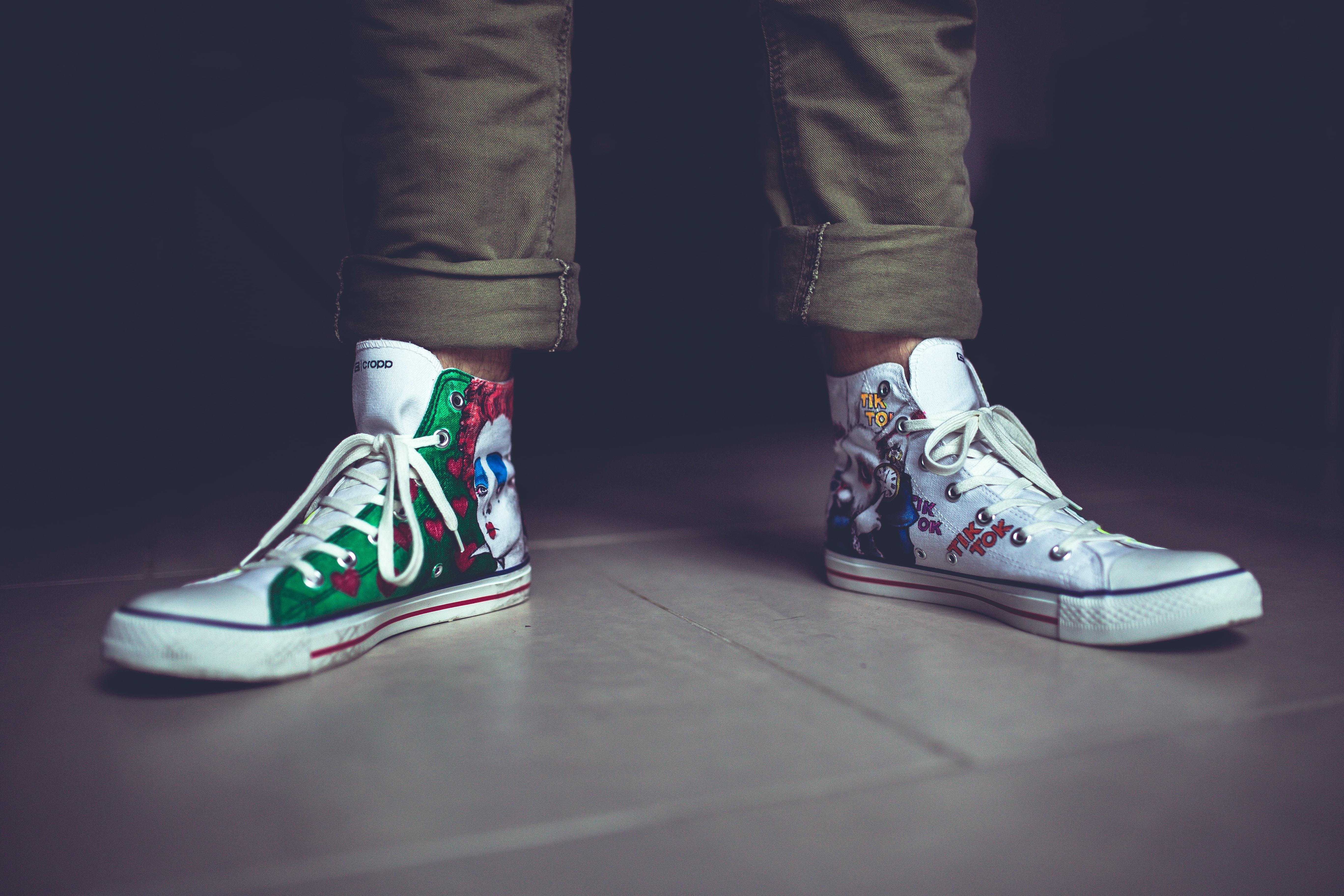 A person's feet wearing a pair of hi-tops covered in colourful graphics, with long laces.